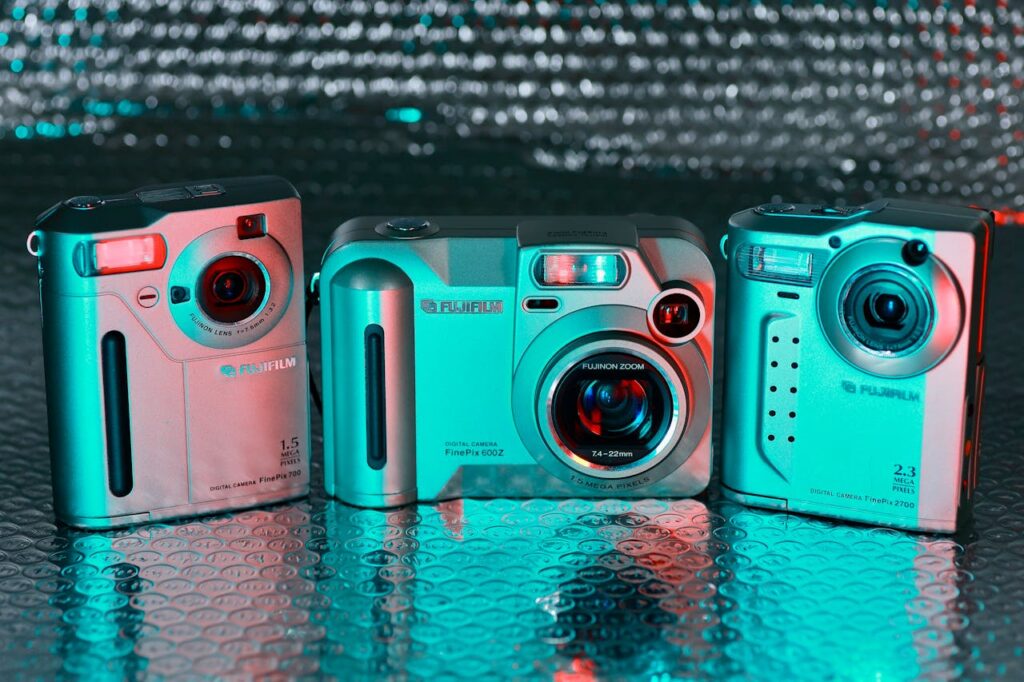 Three vintage digital cameras with vibrant red and teal lighting on reflective surface.