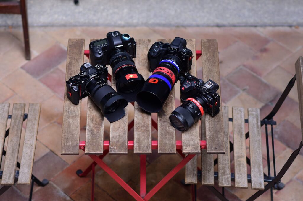 A variety of DSLR cameras arranged on a rustic wooden table outdoors.