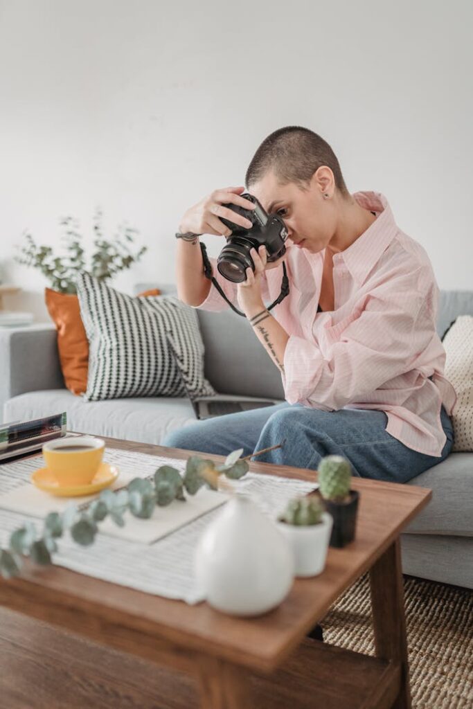 Serious short haired female photographer sitting on sofa and shooting photo of cup of coffee placed on table